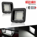 A pair of F150 License plate lights of black housing with clear lens. Two black square LED license plate light bulbs for Ford F150 2015 and up, shown on a white background with a small diagram and illuminated inset photos demonstrating use.