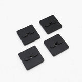 Four black square buttons with central holes on a white background