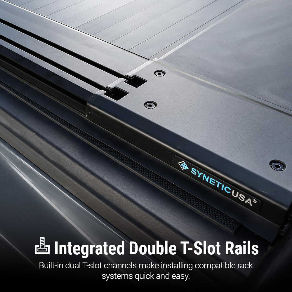 Close-up of a black SyneticUSA truck bed accessory with integrated double T-slot rails, showing the branded panel and text overlay about installed rack compatibility.