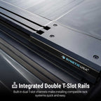Close-up of a black SyneticUSA truck bed accessory with integrated double T-slot rails, showing the branded panel and text overlay about installed rack compatibility.