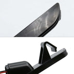 Close-up of a black plastic automotive light assembly, showing the lens edge marked SAE and DOT, and the mounting bracket and wiring connector against a white background.