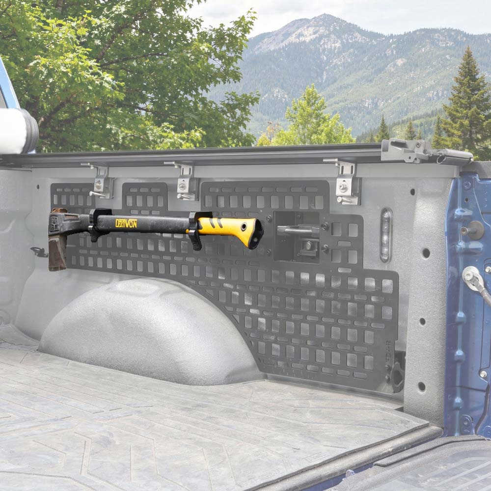 A black and yellow DOWNS firearm rack mounted on the tailgate of a pickup truck, shown outdoors with mountains and trees in the background.