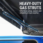 Close-up of a black hardtop tent canopy attached to a blue vehicle, showing a heavy-duty gas strut support arm with overlaid marketing text reading 'HEAVY-DUTY GAS STRUTS' and supporting copy.