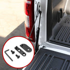 A black metal tailgate support brace installed on the rear edge of a white pickup truck bed, with an inset circle showing the included mounting hardware.