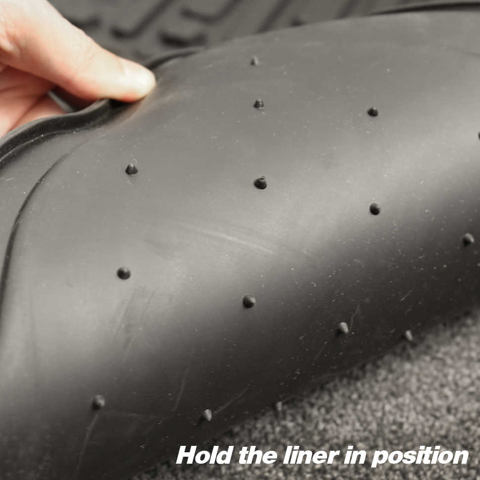 Close-up of a black rubber vehicle liner with small raised nubs, being held by a hand to show flexibility, with the text 'Hold the liner in position' at the bottom.