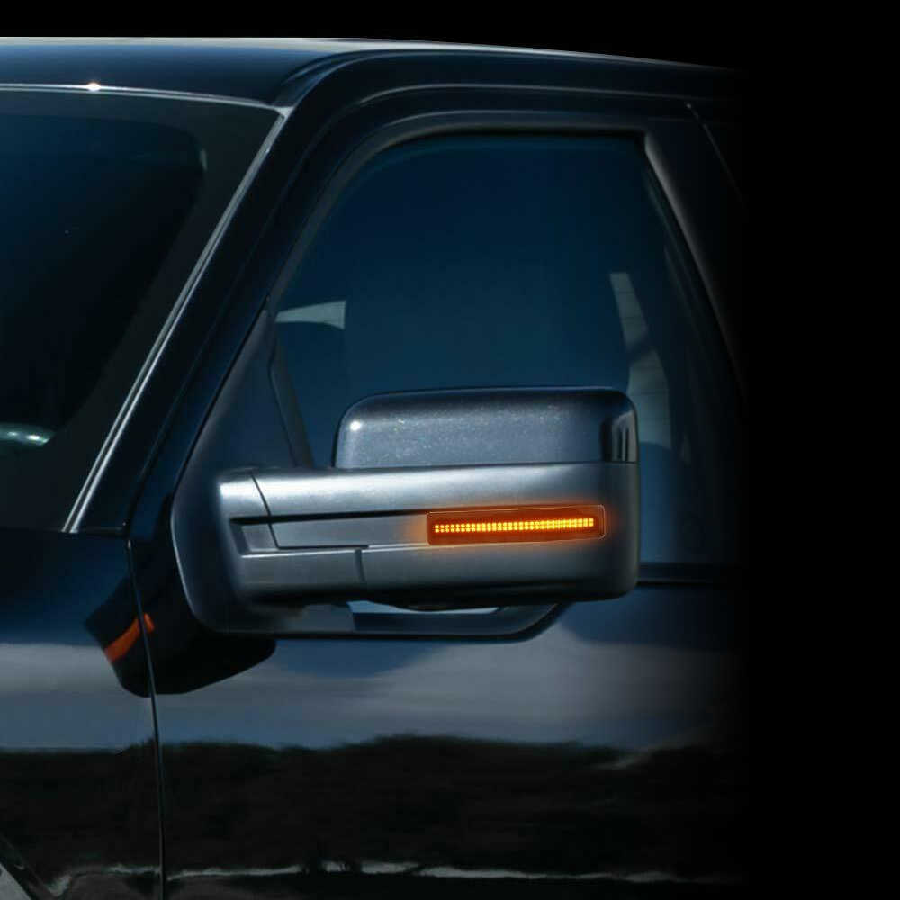 Close-up of a vehicle side mirror with an illuminated amber side marker light, mounted on a dark car body.