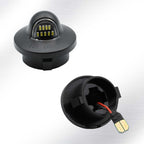 A pair of black automotive LED marker lights shown on a light gray gradient background, with one light displaying the dome-shaped LED lens and the other showing the open back with internal wiring and a connector plug.