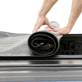 Person unrolling a black and gray mat or rug onto a surface.