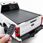 A black roll-up truck bed cover installed on the bed of a white Ford Super Duty pickup truck, shown with a hand holding a key fob in the foreground against a clean white studio background.