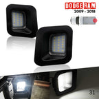 License plate light assembly for RAM 2009-2018. Two black square LED vehicle light badges shown on a white background, with a small car diagram and a Dodge Ram 2009-2018 logo. A lower strip shows the lights illuminated in a vehicle interior.
