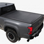 A black tonneau cover installed on the bed of a dark gray pickup truck.
