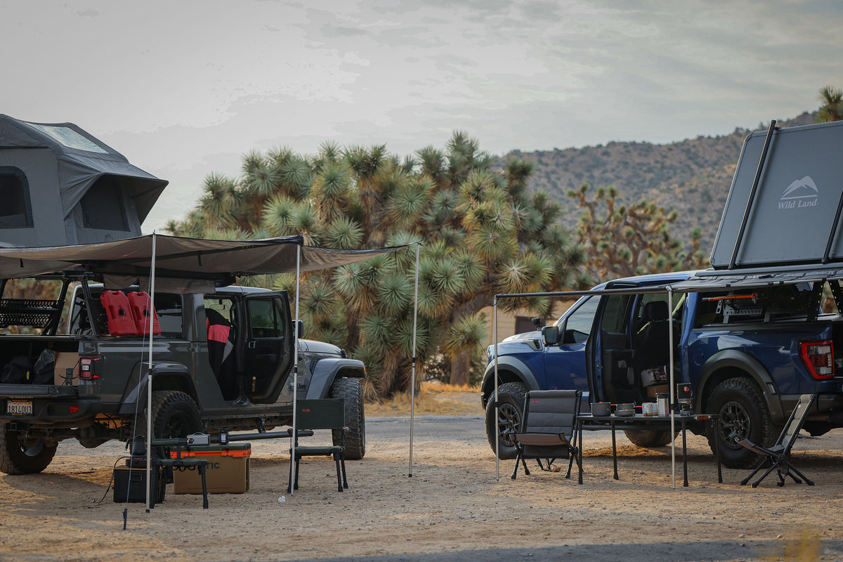 Two vehicles with rooftop tents parked in a desert setting with trees and mountains in the background.