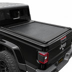 A black retractable bed cover installed on the bed of a black Jeep.

