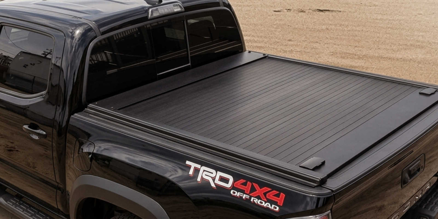 Black truck with a tonneau cover and TRD Off Road badge against a beige wall.