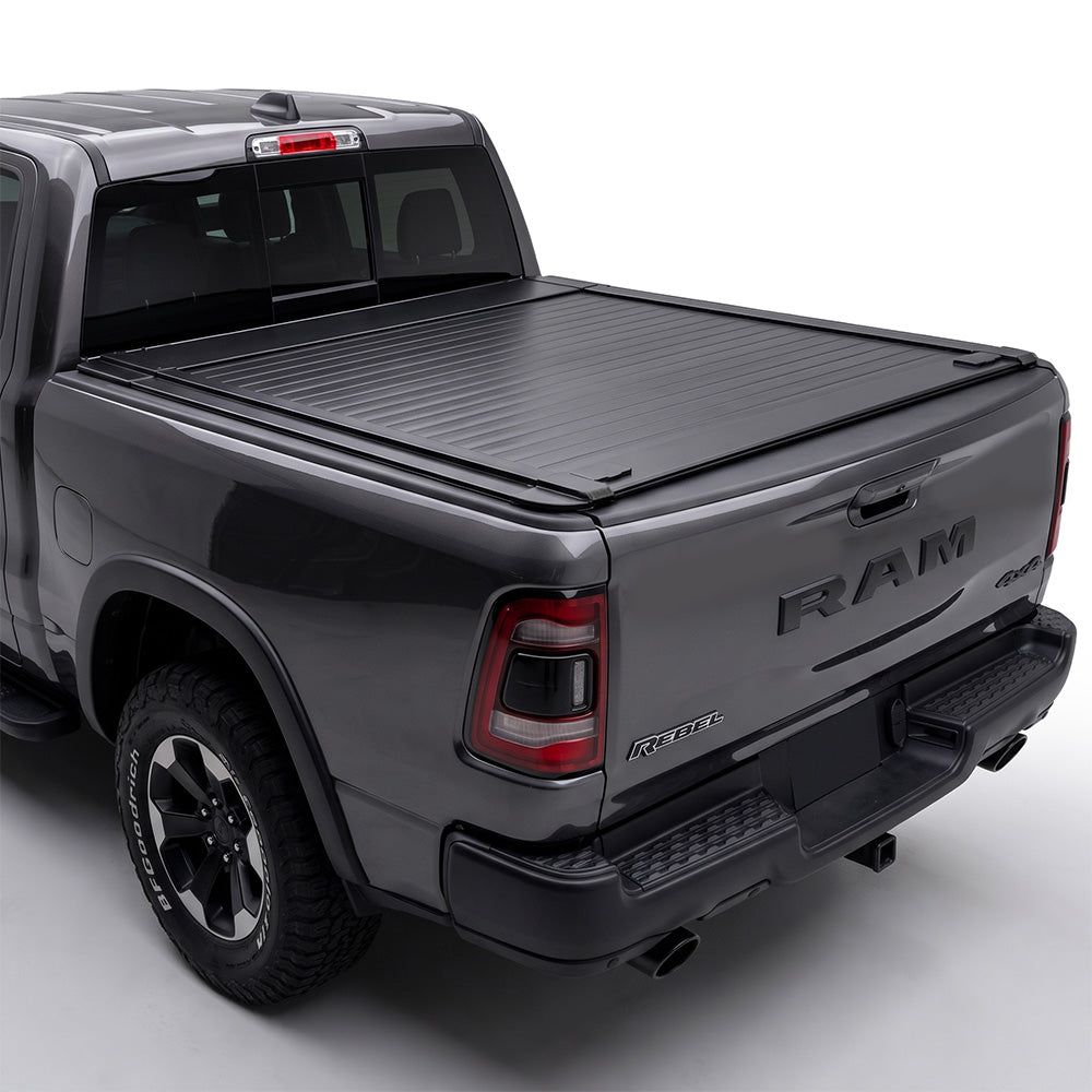 A black retractable truck bed cover installed on the bed of a dark gray Ram pickup truck.